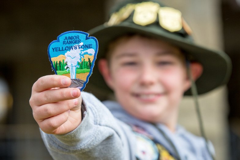 A boy holding up his Junior Ranger badge at Yellowstone National Park © National Park Service