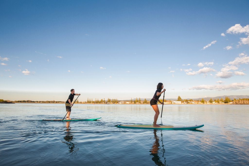 Visitors enjoying a stand up paddleboarding on Lake Illawarra near Wollongong. Image Destination NSW