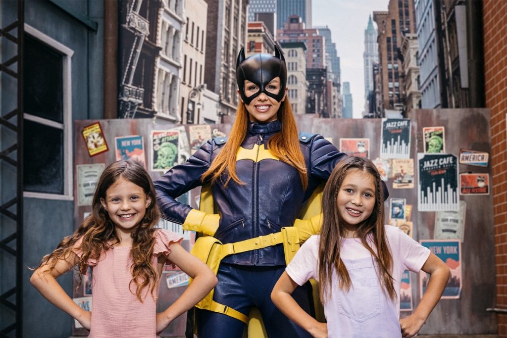 Kids pose with Batgirl at Movie World's DC Super Heroes and Super Villains event. Image Village Roadshow Theme Parks