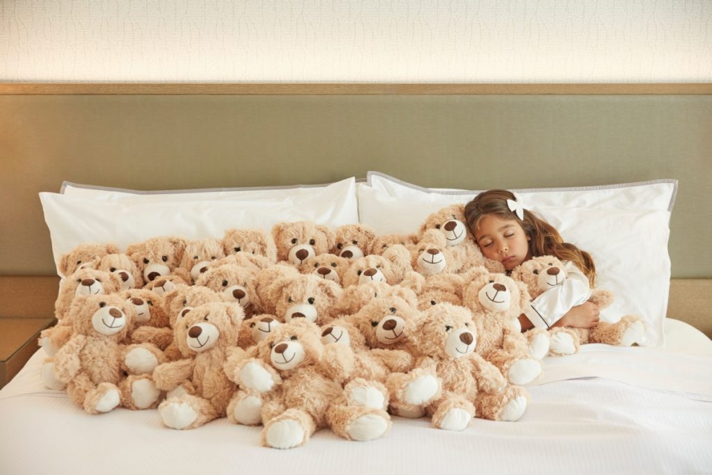 Girl sleeping in hotel room with teddies VisitAnaheim